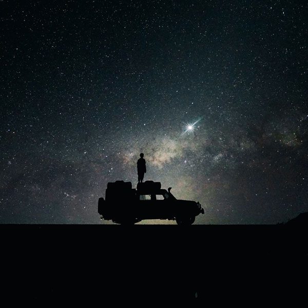 Silhouette of a person standing on top of a jeep with a starry sky behind them